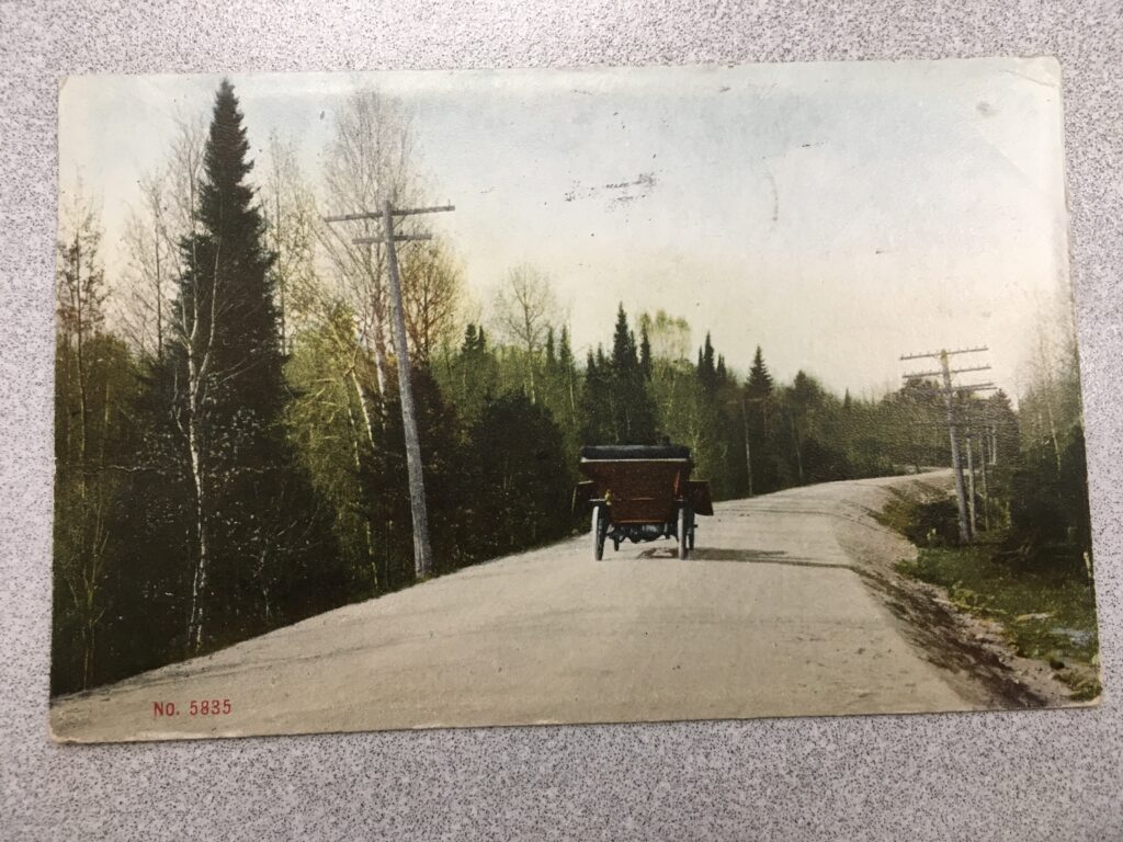 An early 20th century automobile driving along a road lined with electricity or telephone poles.