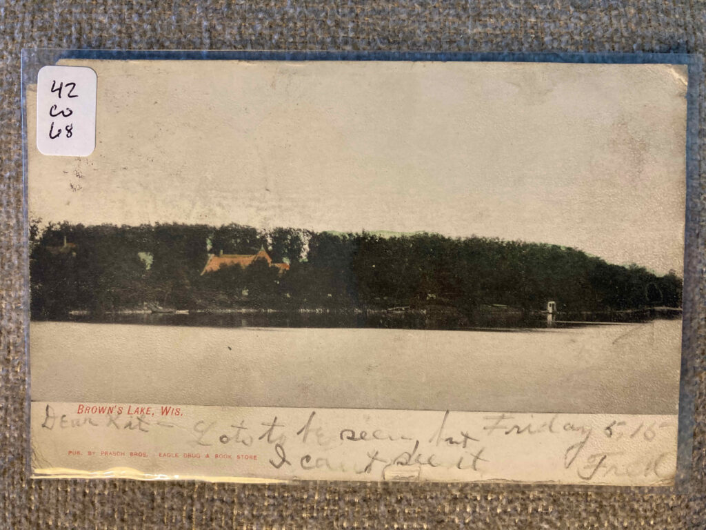 Image of Brown's Lake, Wisconsin, with a roof visible among the trees lining the shore. Message: "Friday 5.15 Dear Kit-- Lots to be seen, but I cant see it Fred"